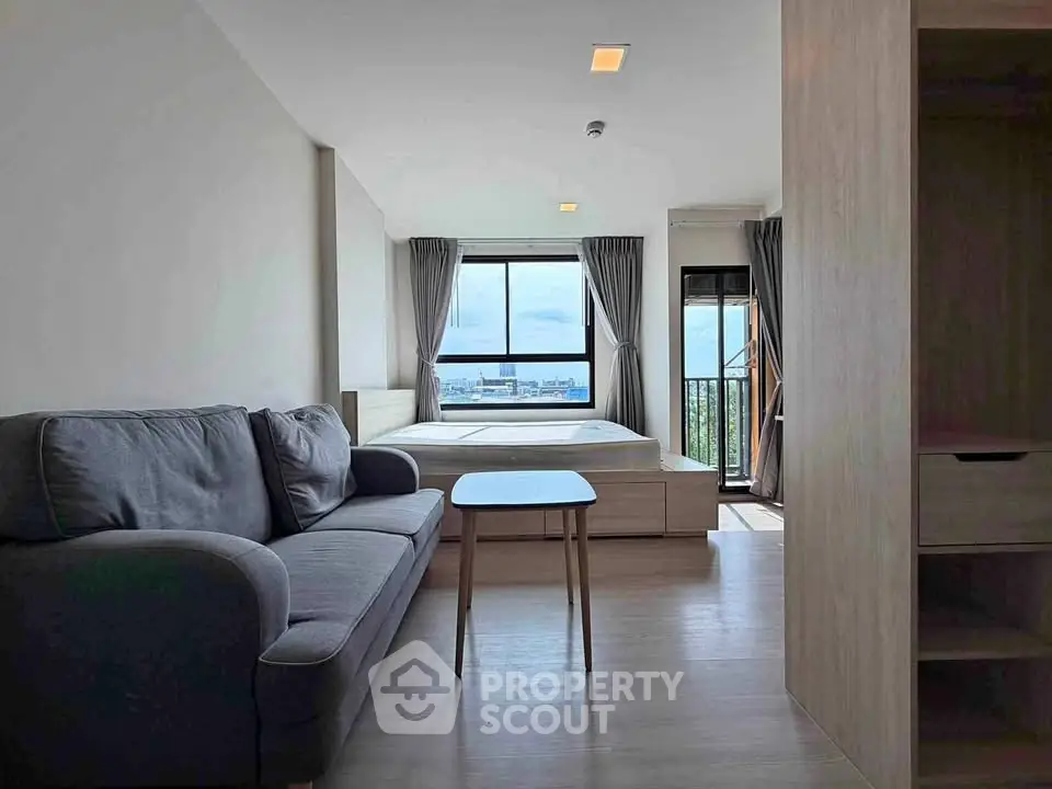 Modern studio apartment with cozy living area and stunning city view from large windows.