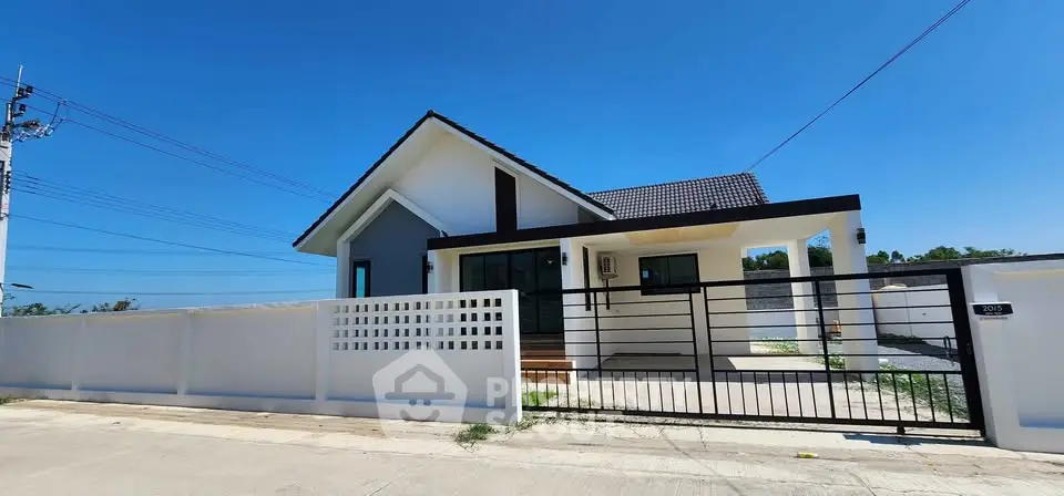 Modern single-story house with gated entrance and spacious driveway under clear blue sky.