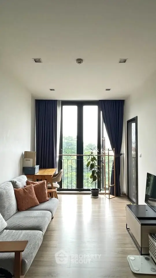 Bright living room with large windows and balcony overlooking greenery, featuring modern furniture and decor.