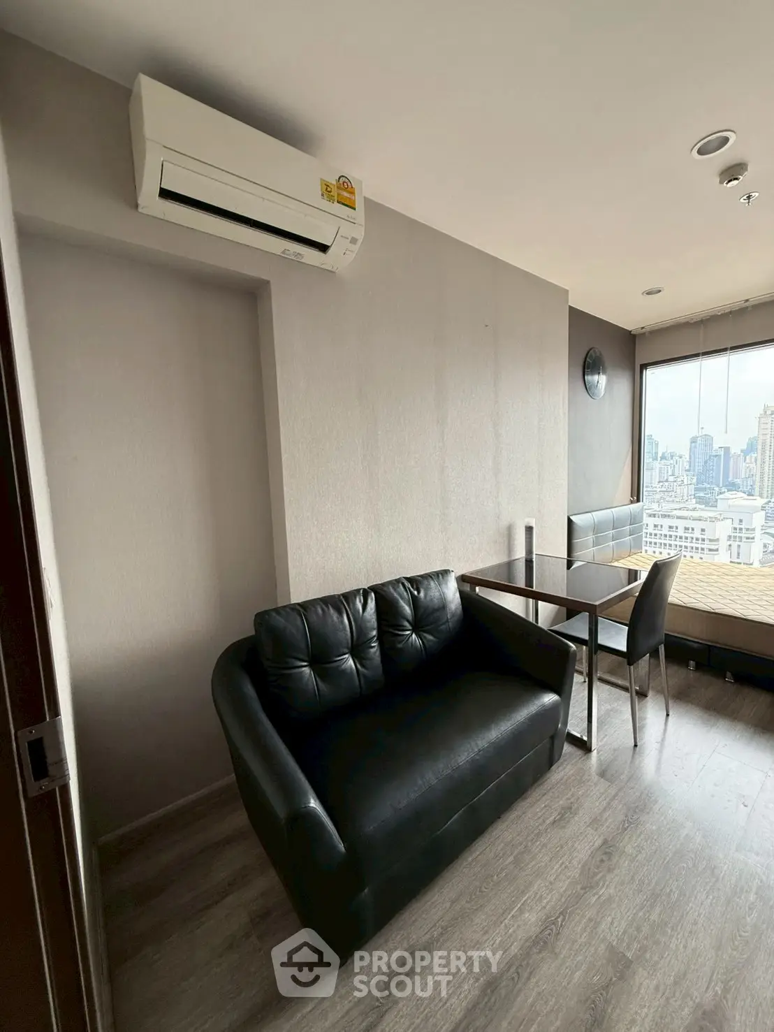 Modern studio apartment with city view, featuring sleek black sofa and dining area.