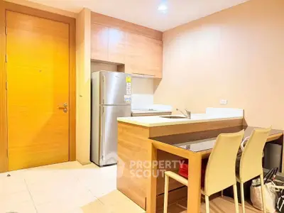 Modern kitchen with sleek wooden cabinetry and stainless steel fridge in cozy apartment.