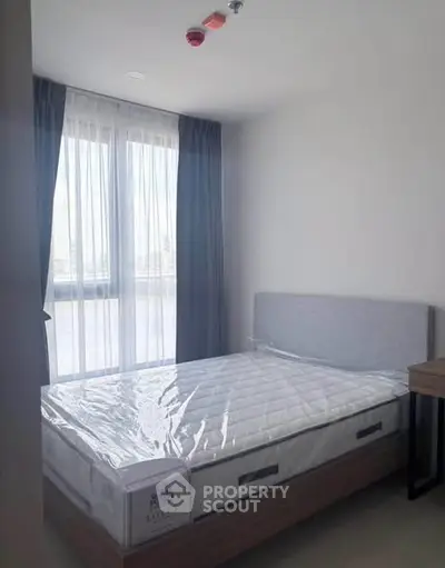 Modern bedroom with large window and natural light, featuring a new mattress and stylish decor.