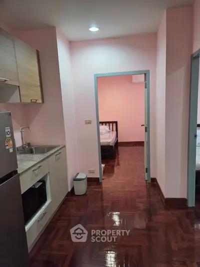 Cozy apartment interior with kitchen and bedroom view, featuring wooden flooring and modern appliances.
