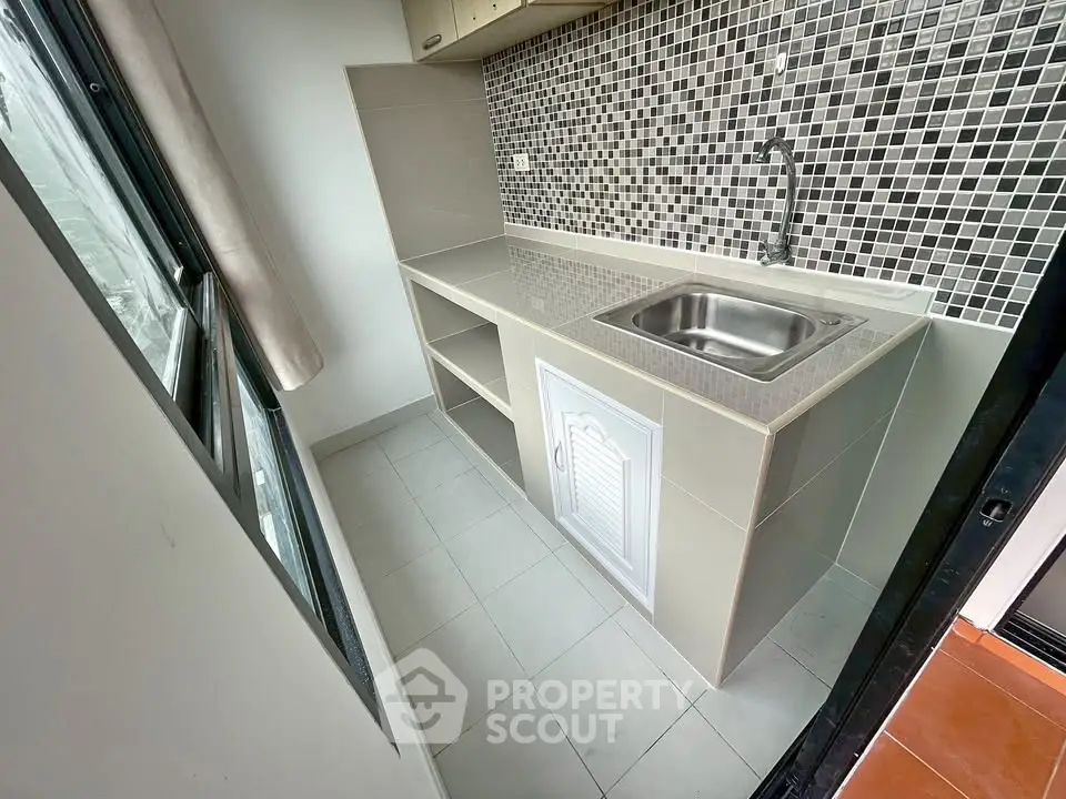 Compact kitchen with mosaic backsplash and stainless steel sink in modern apartment.