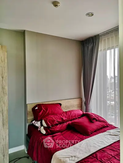 Cozy bedroom with red bedding and large window offering city views, perfect for urban living.