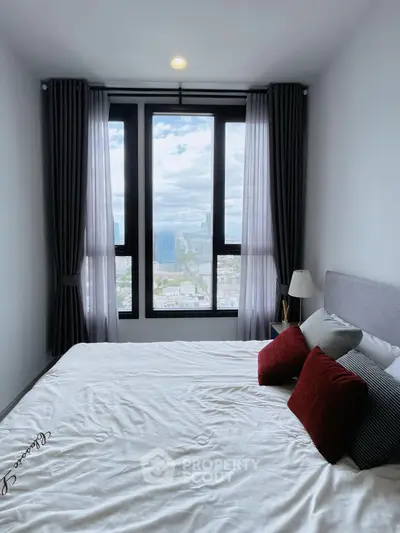Modern bedroom with large window offering stunning city view, elegant decor and cozy ambiance.
