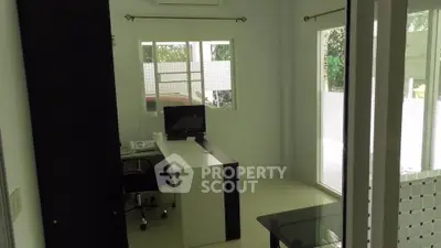 Modern home office with sleek desk and computer setup, featuring large windows for natural light.