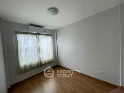 Spacious empty bedroom with wooden flooring and large window, perfect for customization.