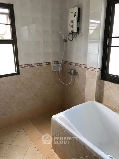 Spacious bathroom with bathtub and modern shower heater, featuring tiled walls and natural light.