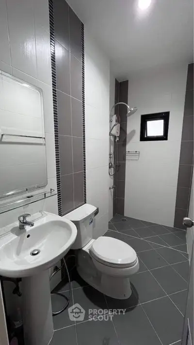 Sleek modern bathroom with a walk-in shower, pedestal sink, and wall-mounted mirror, featuring stylish gray tiling and a minimalist design.