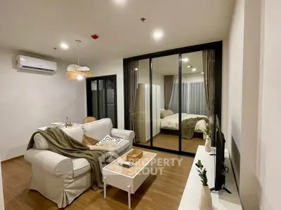 Modern open-plan living room with cozy bedroom view, stylish decor, and wooden flooring.