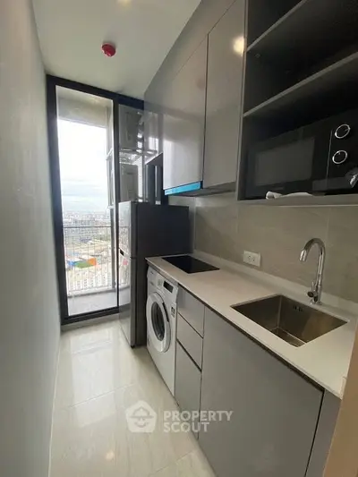 Modern compact kitchen with sleek cabinetry and appliances, featuring a washing machine and microwave.
