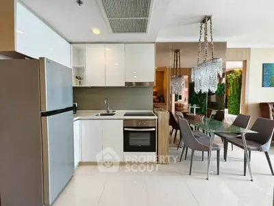 Modern kitchen with sleek white cabinets and dining area featuring elegant chandelier.