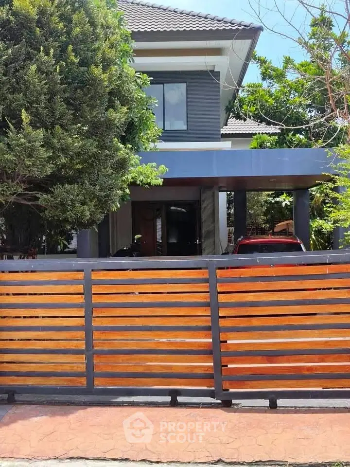 Modern two-story house with sleek design and gated entrance, surrounded by lush greenery.
