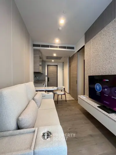 Modern living room with sleek design and open kitchen layout, featuring a cozy sofa and flat-screen TV.