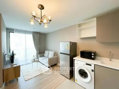 Modern living room with open kitchen, featuring washing machine and fridge, bright natural light.