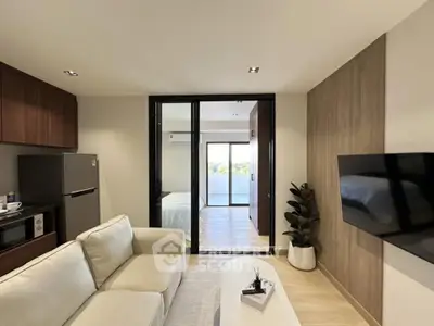 Modern living room with open layout, featuring a cozy sofa, wall-mounted TV, and view into a bright bedroom.
