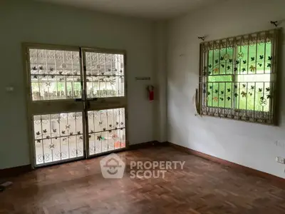 Spacious room with wooden flooring and decorative window grills, ideal for customization.