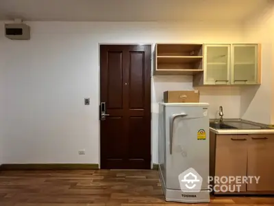 Compact kitchen area with wooden cabinets and fridge in modern apartment