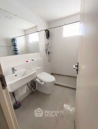 Modern bathroom with sleek fixtures and large mirror, featuring a spacious shower area and natural light.