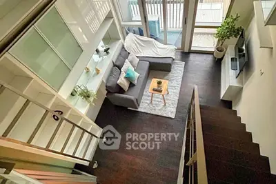 Modern loft-style living room with high ceilings and large windows, featuring a cozy sofa and stylish decor.