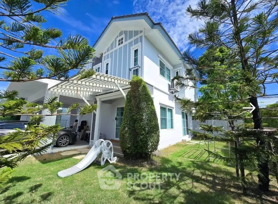 Charming two-story white house with lush garden and outdoor slide, perfect for family living.