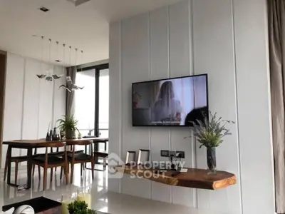 Modern living room with elegant dining area and wall-mounted TV, featuring sleek decor and natural light.