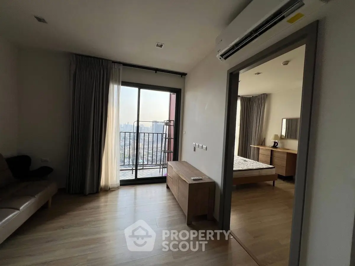 Modern apartment with balcony and bedroom view, featuring sleek furniture and cityscape.