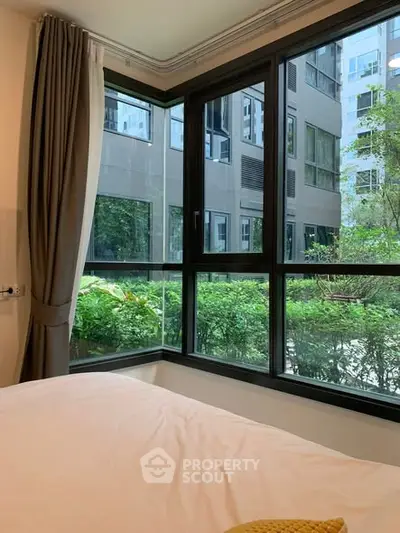 Bright bedroom with large windows offering a lush garden view in a modern apartment.