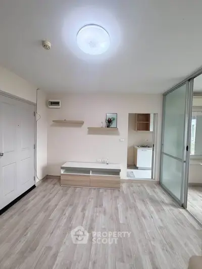 Modern living room with light wood flooring and sliding glass doors, leading to a bright laundry area.