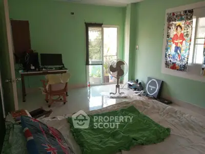 Spacious bedroom with green walls, featuring a computer desk and a fan, offering a cozy and functional living space.