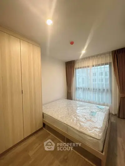 Cozy bedroom with wooden wardrobe and large window with curtains, perfect for relaxation.