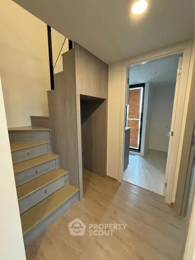 Modern interior with wooden staircase and hallway leading to a bright room.