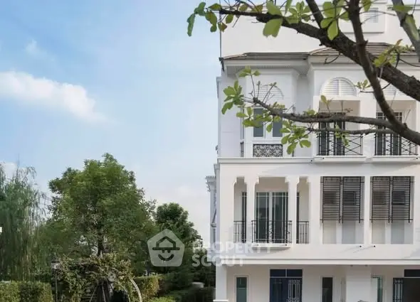 Elegant white building exterior with lush greenery and clear blue sky.