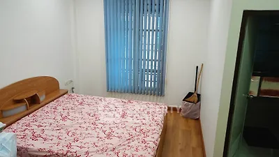 Cozy bedroom with wooden flooring and floral bedspread, featuring vertical blinds on the window.