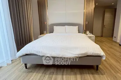 Spacious bedroom with modern decor and wooden flooring, featuring a comfortable bed and elegant curtains.