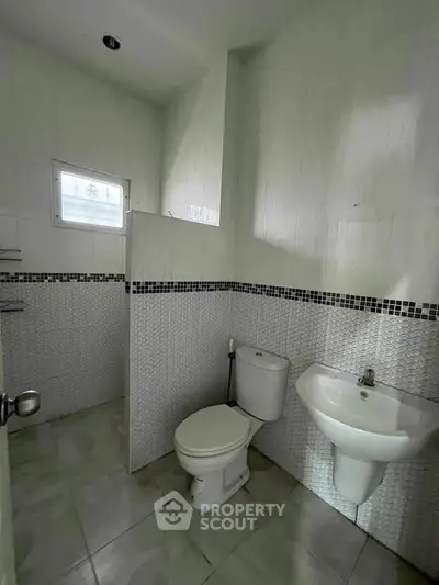 Modern bathroom with sleek white tiles and compact design, featuring a toilet and wall-mounted sink.