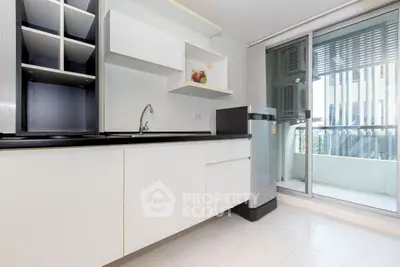 Modern kitchen with sleek white cabinets and balcony access in urban apartment.