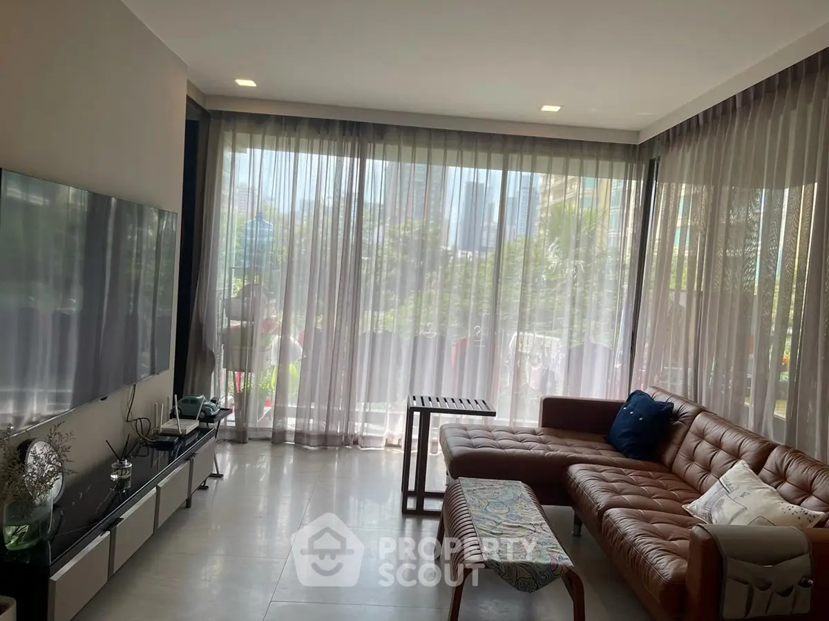 Spacious living room with modern decor and large windows offering a lush garden view.
