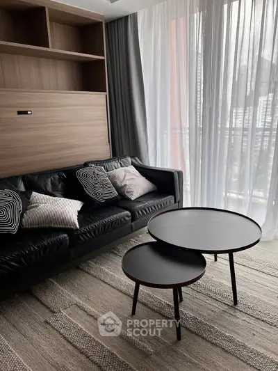 Modern living room with stylish black leather sofa and nested coffee tables, featuring floor-to-ceiling windows.