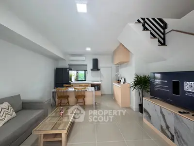 Modern open-plan living room with sleek kitchen and stylish staircase in a contemporary home.