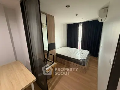 Modern bedroom with wooden flooring and large window, featuring a bed and study desk.