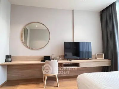 Modern bedroom with stylish desk, large TV, and round mirror, perfect for a cozy and functional living space.