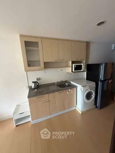 Modern kitchen with wooden cabinets, washing machine, and fridge in a compact layout.