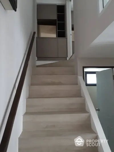 Modern staircase with wooden steps and sleek handrail leading to upper floor