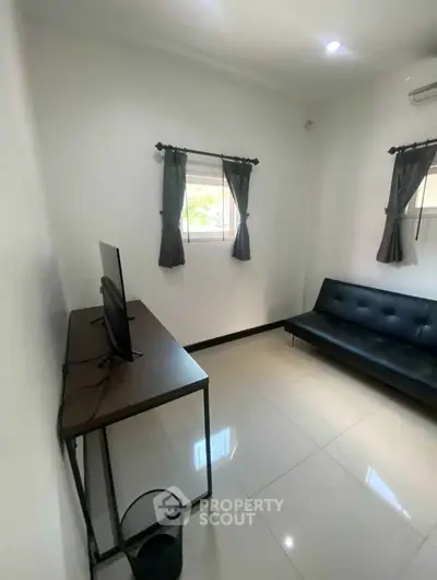 Modern living room with sleek black sofa and wall-mounted TV, featuring minimalist decor and natural light.