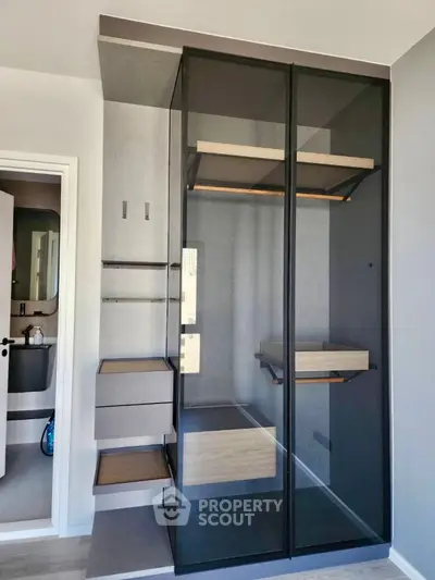 Modern minimalist walk-in closet with sleek glass doors and wooden shelves.