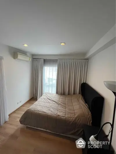 Spacious and well-lit bedroom with a large window draped in elegant curtains, featuring a comfortable bed and modern air conditioning unit.