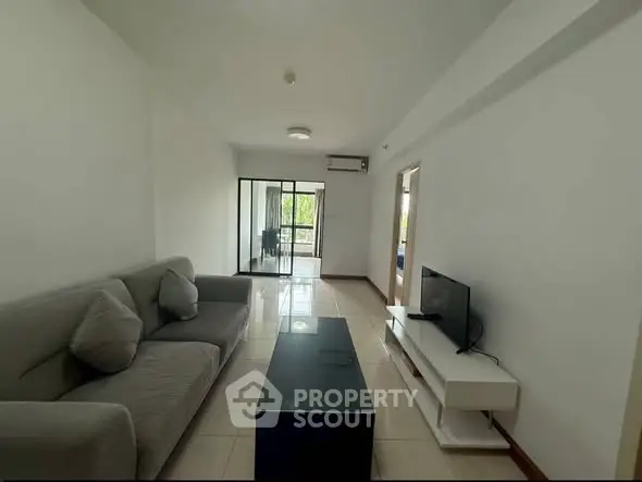 Spacious living room with modern sofa and TV, leading to a bright balcony view.