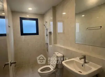 Modern bathroom with sleek fixtures and neutral tiles, featuring a window for natural light.